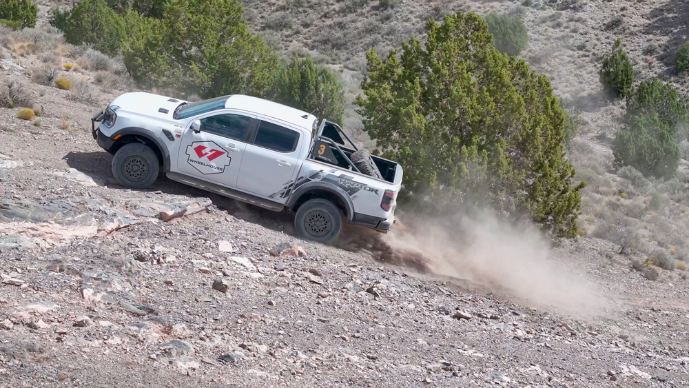 Ford Ranger Raptor blanc gravissant une pente rocheuse à Five Mile Pass, avec de la poussière derrière ses roues arrière