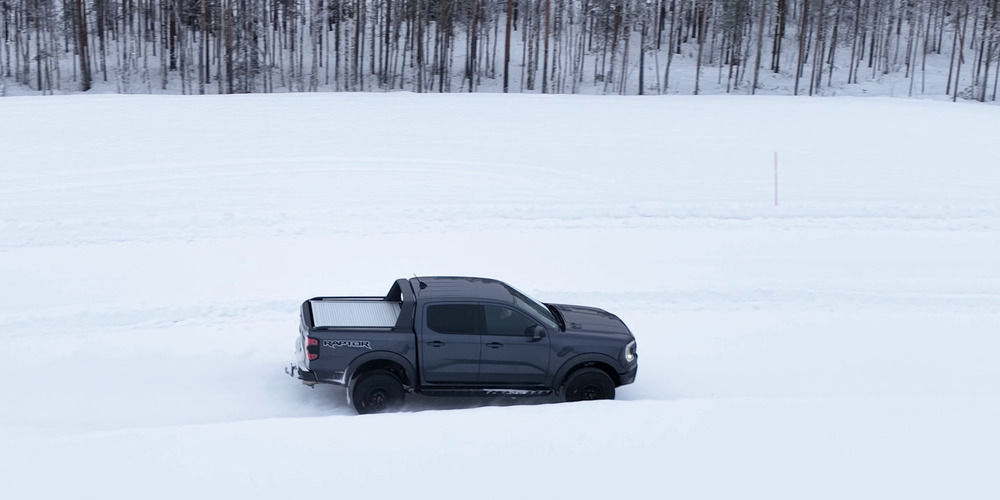 Ford Ranger Raptor gris roulant sur un circuit d'essai enneigé en bordure de forêt
